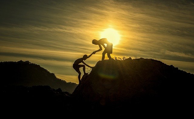 una persona ayudando a otra a subir una montaña, dándole la mano